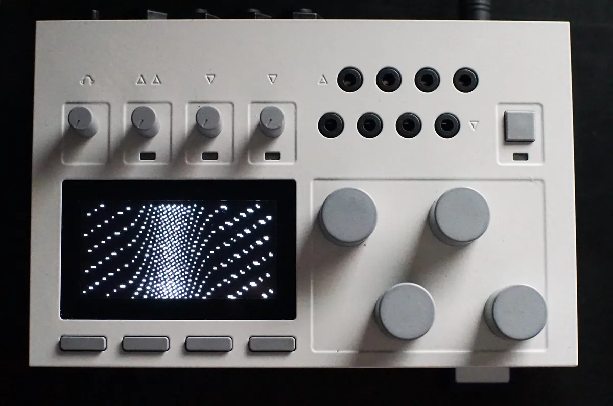 Cream and grey electronic instrument on a dark ground, knobs and a pixel display under one soft highlight